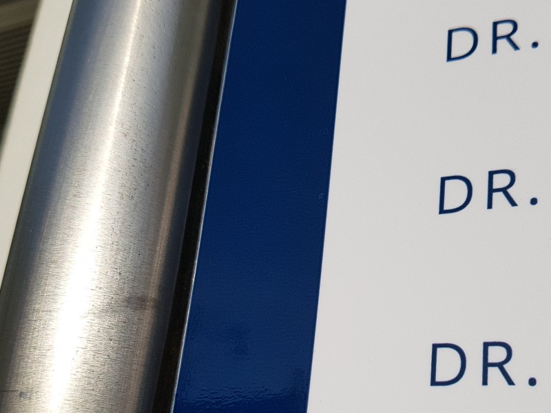 Auf dem Foto ist der Ausschnitt eines Schildes zu sehen, bei dem untereinander dreimal die Buchstaben D & r für Doktor stehen.