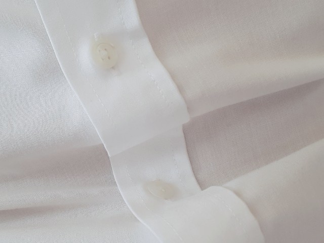 Das Foto zeigt die Knopfleiste eines weißen Hemdes, leicht in Wellen gelegt.