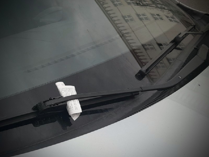 Das Foto zeigt einen unter dem Scheibenwischer eines Autos angebrachten Strafzettel.