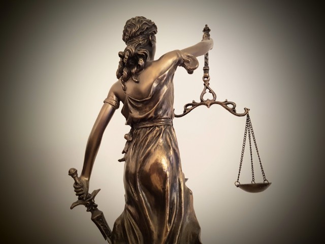 Das Foto zeigt einen von hinten fotografierte Justitia, welche Recht und Gerechtigkeit symbolisiert, das ist zu erkennen, dass sie in der rechten Hand die Waage und in der linken Hand ein Schwert hält.