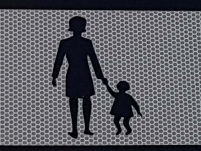 Zu sehen ist die stilisierte Abbildung einer Frau mit Kind in schwarz auf grauem Refexionshintergrund; die Frau hält das zu ihr aufschauende Kind an der Hand.